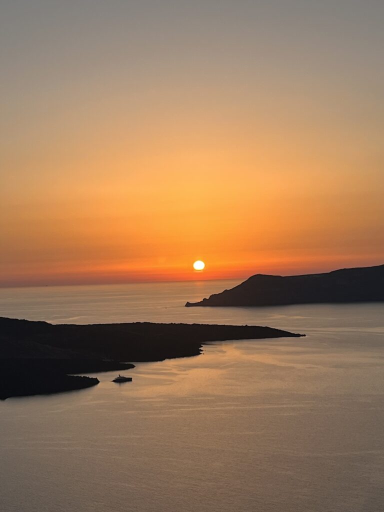 orange sun going down near horizon, with an orange sky and two land forms on either side