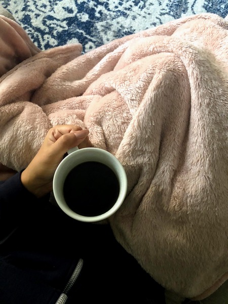 a lesson in how to enjoy your own company, set up a comfortable environment. photo shows woman holding a cup of coffee with a pink fuzzy blanket over her legs