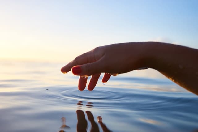 hand dipping fingertips into a pool of water to cause a ripple. represents the ripple effect of ancestral healing