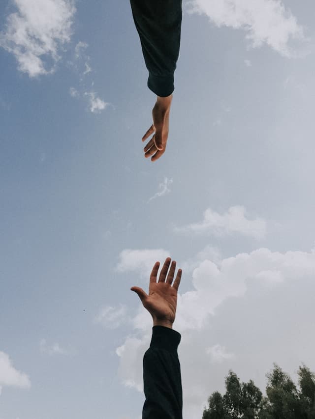 blue sky background with two hands reaching toward each other, one from the top of the photo and one from the bottom