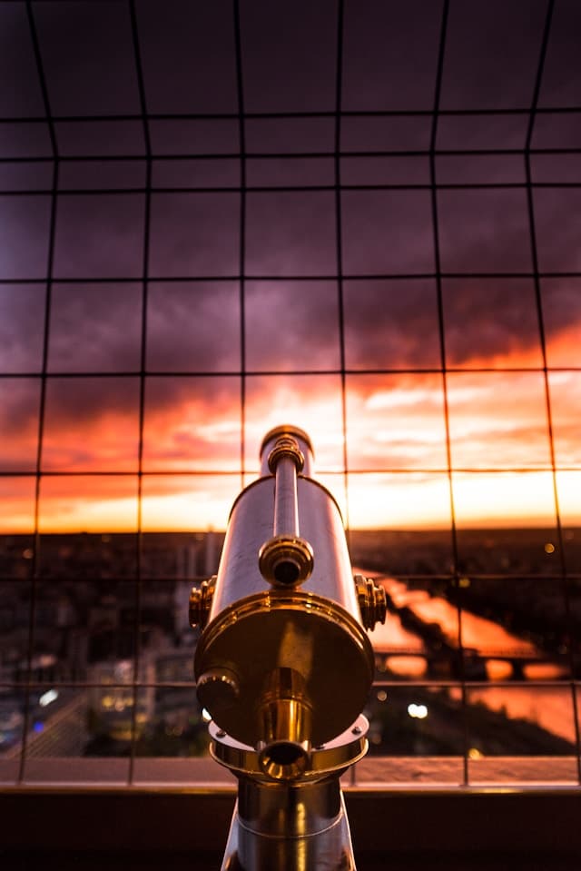 telescope pointing out toward an orange and dark purple sunset in sky