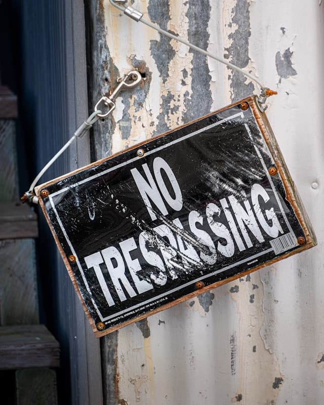 black rectangular sign hanging lopsided from wall reads no trespassing in white letters