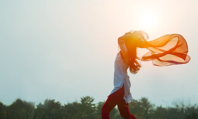 woman running freely holding an orange sheer scarf blowing in the wind